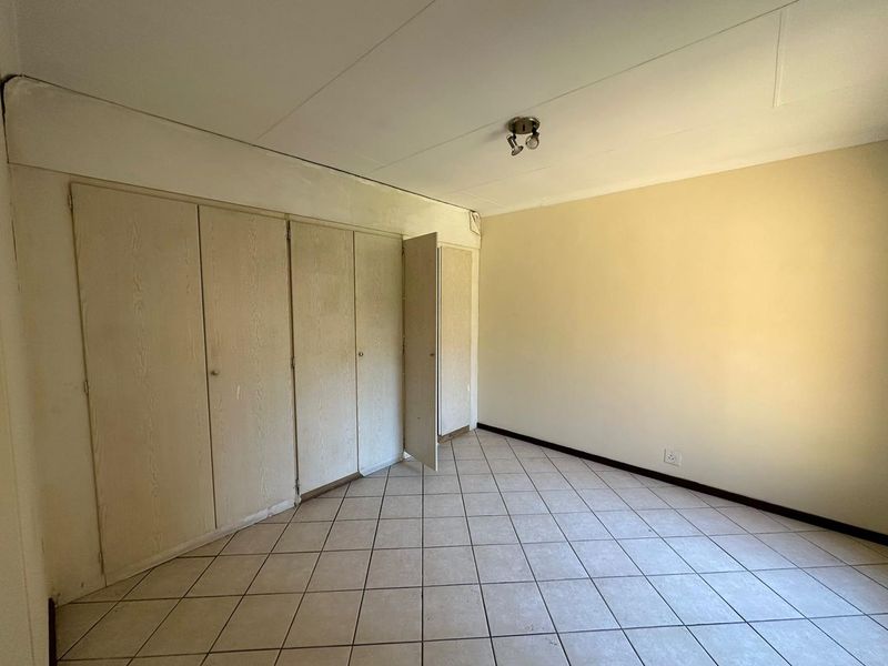 An empty bedroom featuring tiled flooring and extensive built-in cupboard storage, offering a blank canvas for renovation or interior design updates.