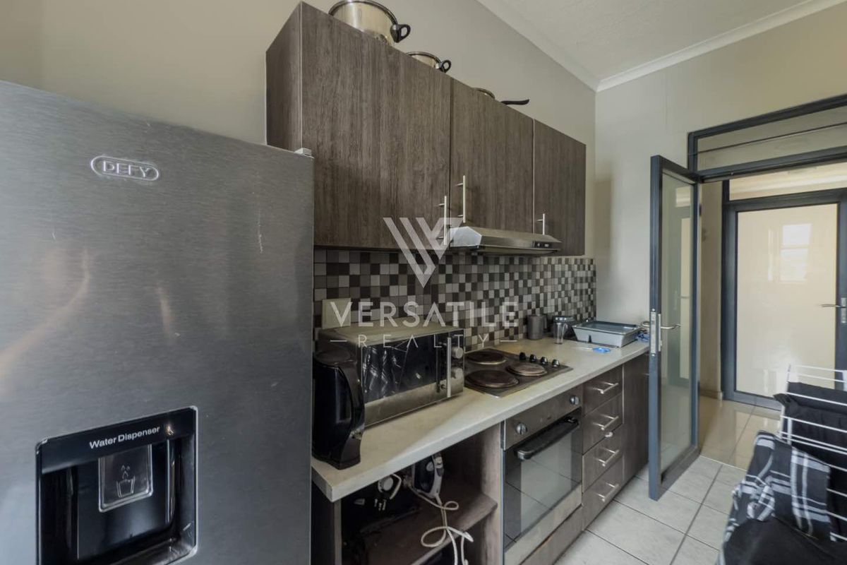 Compact kitchen featuring dark wood-look cabinetry, a tiled backsplash, built-in oven, and hob with an extractor fan.