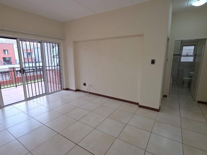 An empty, tiled living area featuring a sliding glass door with a security gate, leading to an outdoor balcony space.