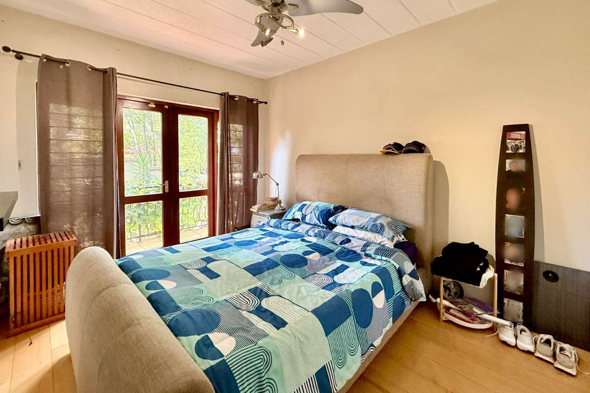 A bedroom featuring light wood-look flooring, a ceiling fan, and double doors providing access to an outdoor balcony area.