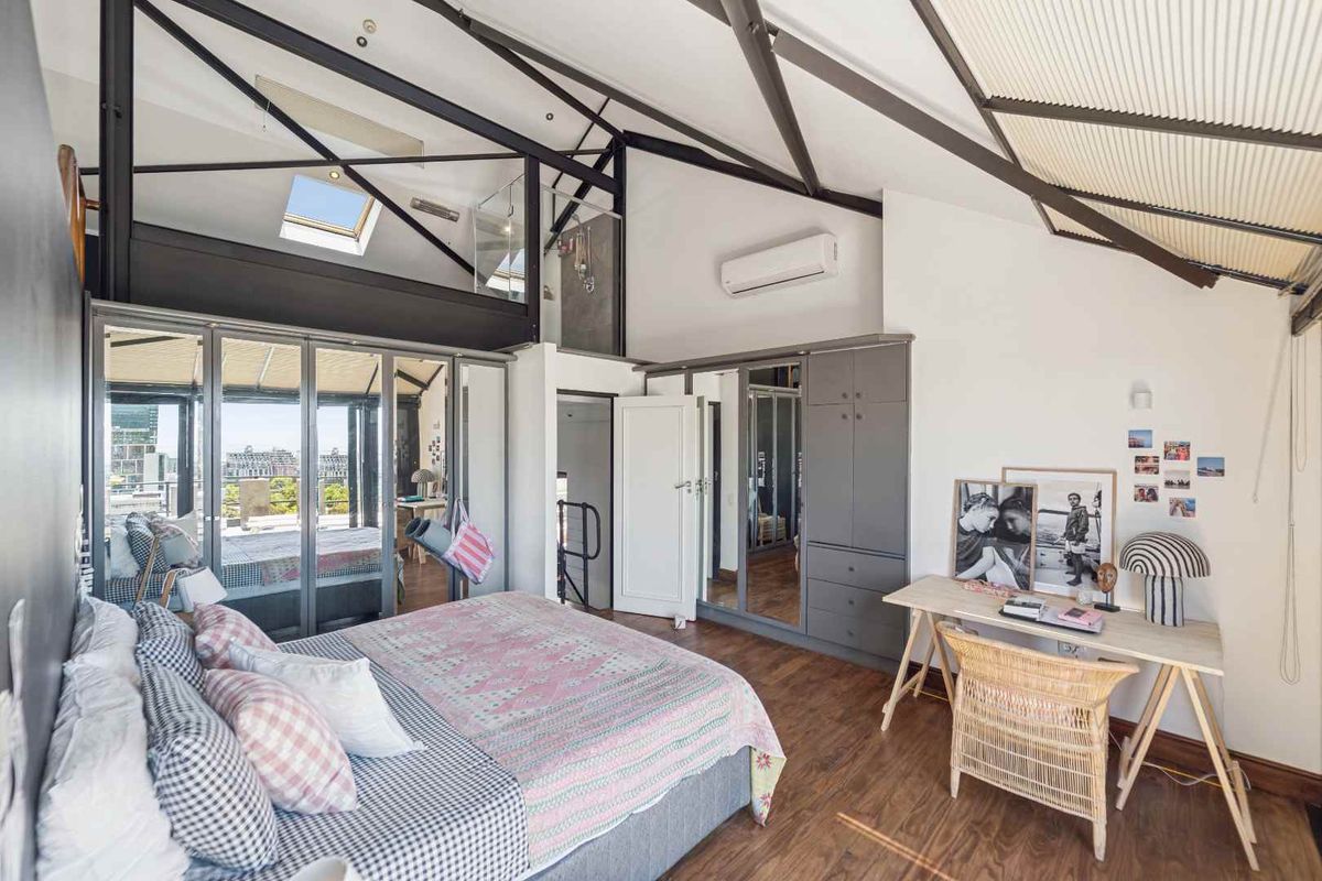 Spacious bedroom featuring high vaulted ceilings with exposed steel trusses, a skylight, built-in cabinetry, and direct access to a balcony through glass sliding doors.