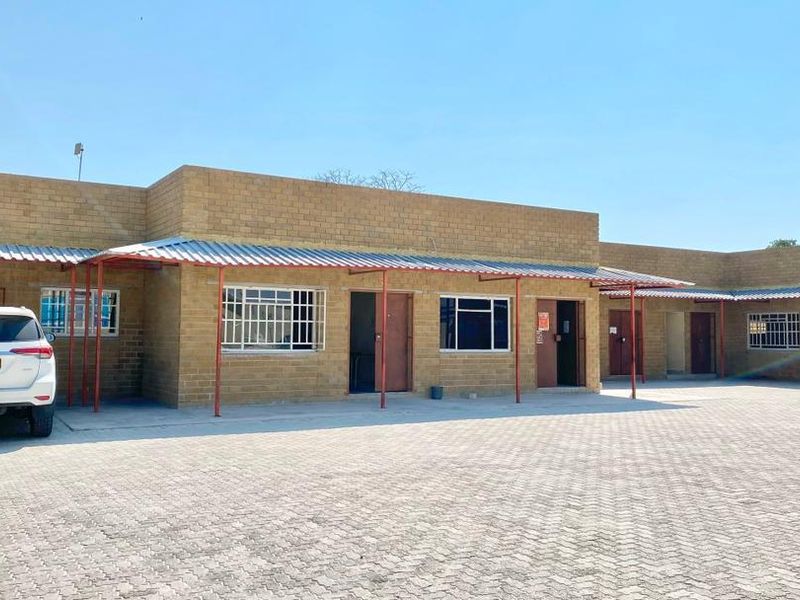 A commercial property featuring a face brick facade, corrugated metal roofing, and a spacious paved driveway area with multiple access points.