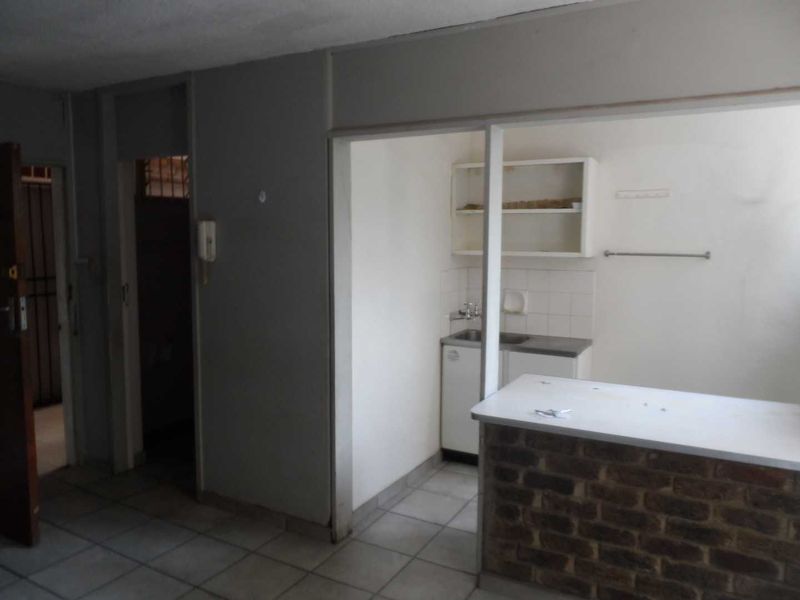 Open plan living area featuring a brick breakfast bar and a compact kitchen with built-in cabinetry and tiled flooring.