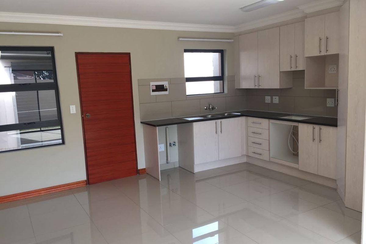 A clean, modern kitchen featuring light-toned built-in cabinetry, dark countertops, a double sink, and polished tiled flooring in an open-plan layout.