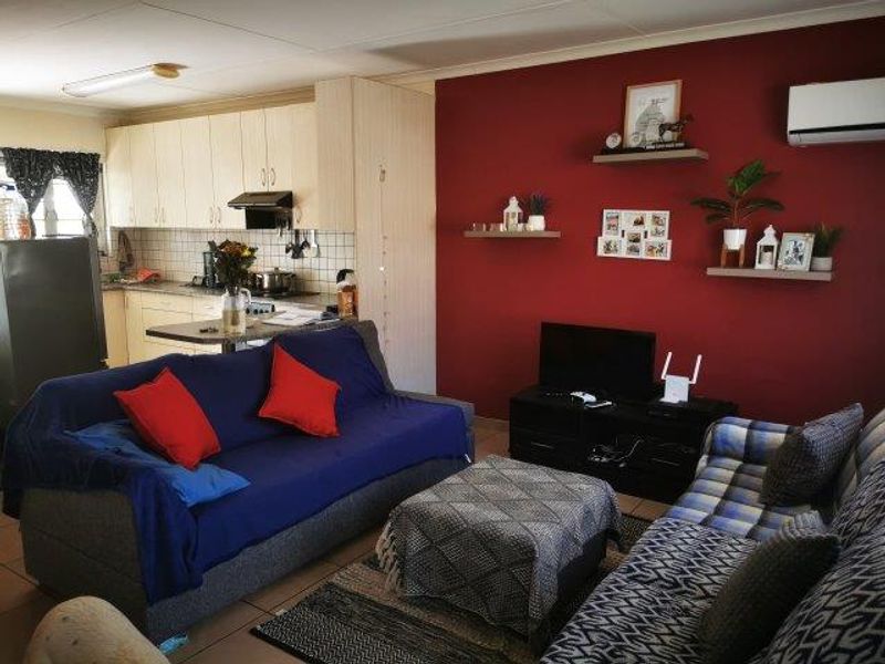 Open-plan living area featuring a functional kitchen with cabinetry and a spacious lounge area with a wall-mounted air conditioning unit.