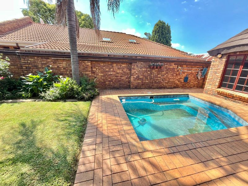 Outdoor pool area featuring a swimming pool surrounded by brick paving, set against a facebrick boundary wall and a tiled roof structure.