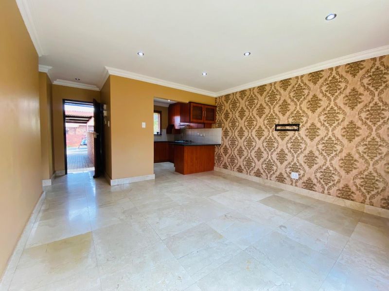 Spacious open-plan living area featuring stone tile flooring, recessed lighting, and a connected kitchen with built-in cabinetry and an extractor fan.