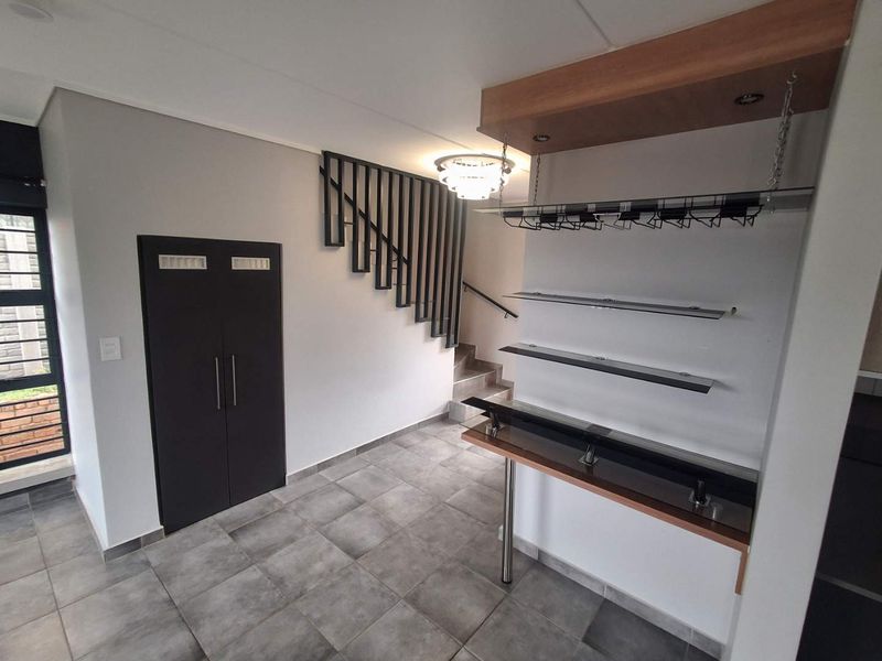 A modern interior space featuring a built-in bar area with glass shelving, a staircase with a metal balustrade, and neutral tiled flooring.