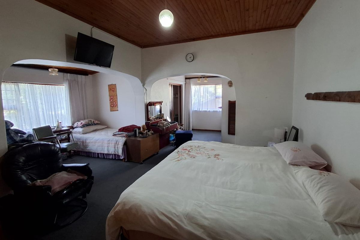 Spacious bedroom featuring a timber tongue and groove ceiling, arched architectural details, and carpeted flooring, offering a versatile layout with an adjoining area.