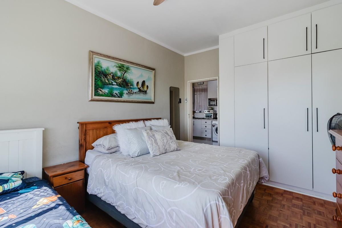 A well-maintained bedroom featuring parquet flooring, built-in floor-to-ceiling white cabinetry, and a view into the adjacent kitchen area.