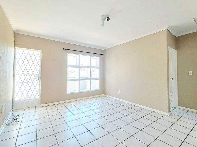 A bright, empty bedroom featuring tiled flooring, a security gate, and a multi-pane window, offering a clean canvas for personalization.