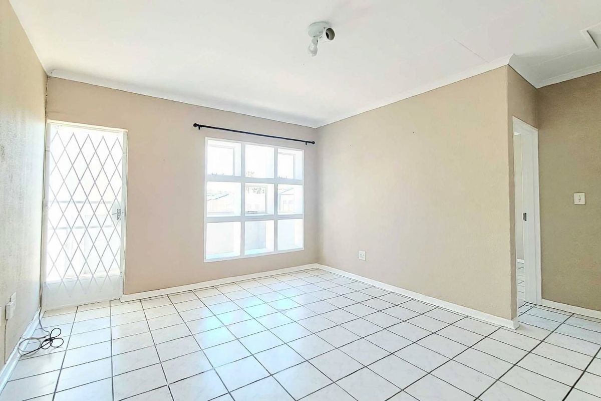 A bright, empty bedroom featuring tiled flooring, a security gate, and a multi-pane window, offering a clean canvas for personalization.
