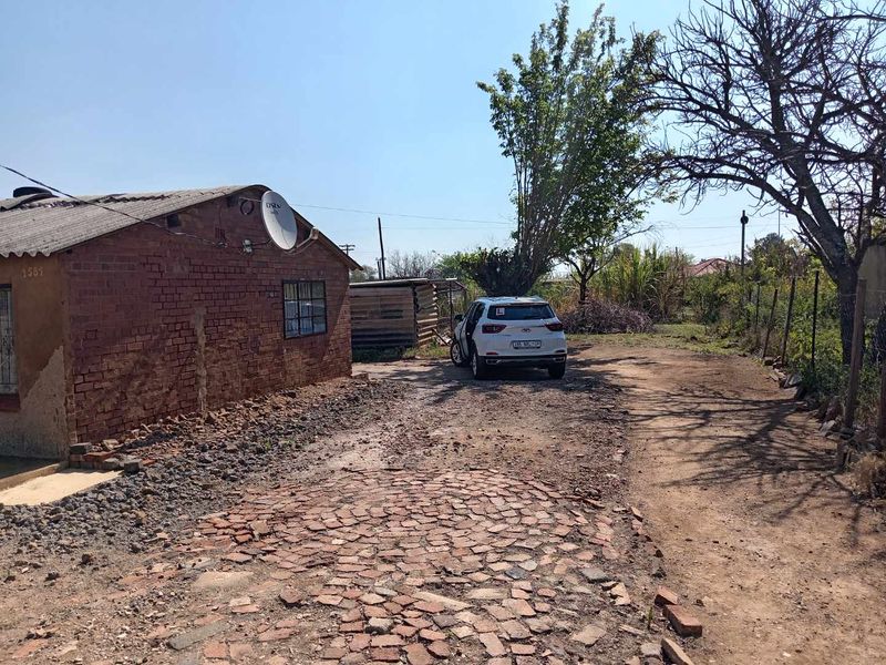 Front exterior view of a brick house featuring a cobblestone driveway and basic perimeter fencing.