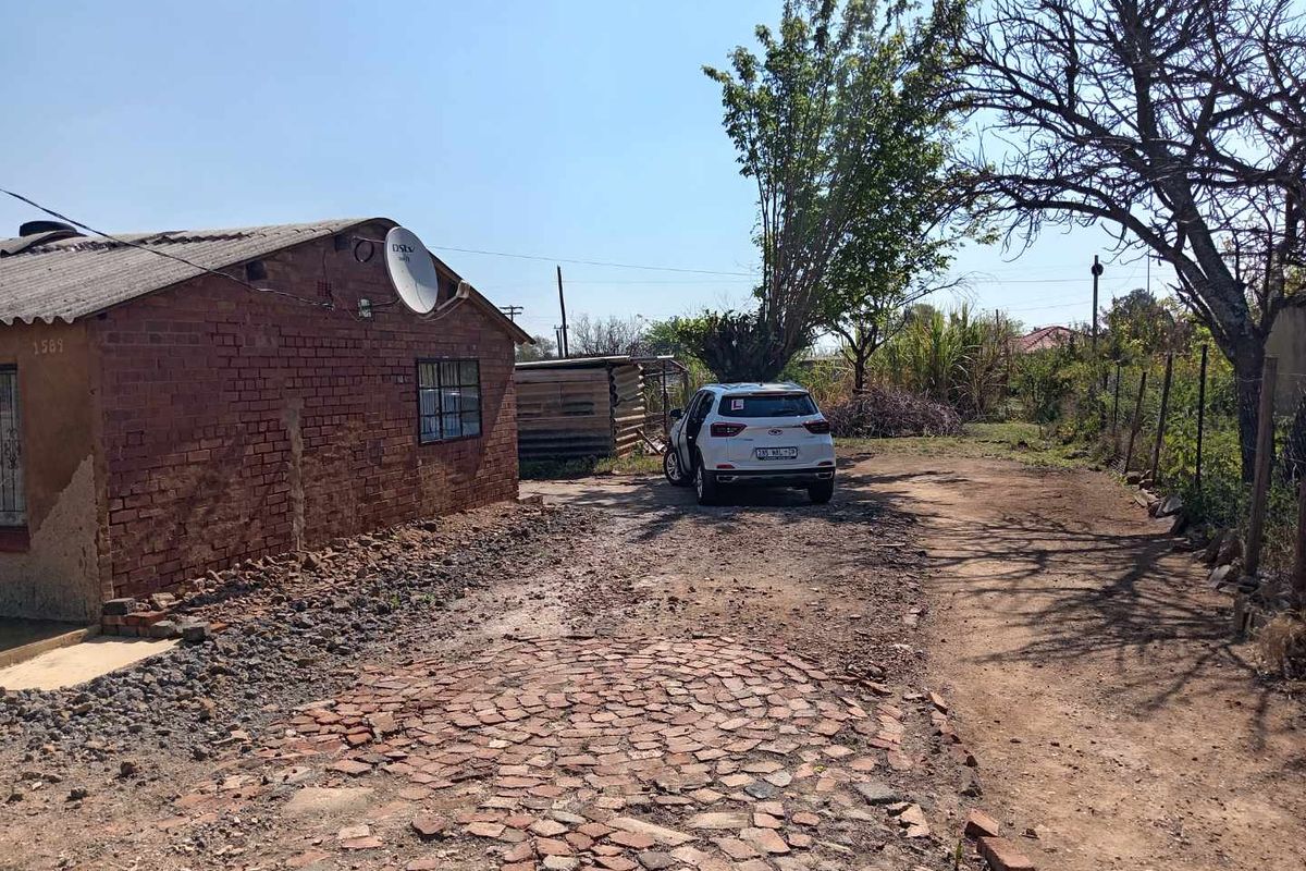 Front exterior view of a brick house featuring a cobblestone driveway and basic perimeter fencing.