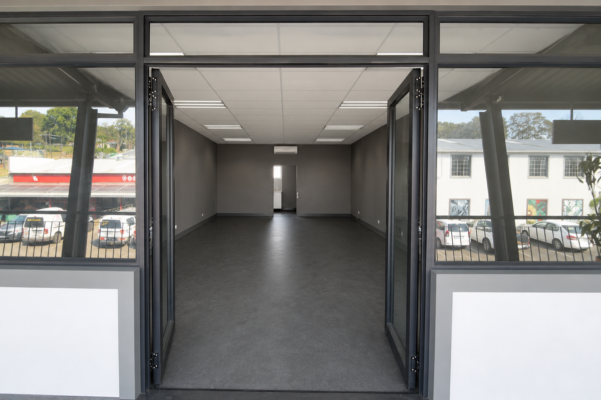 A spacious, modern open-plan commercial unit featuring neutral grey walls, durable vinyl flooring, recessed lighting, and large glass entrance doors.