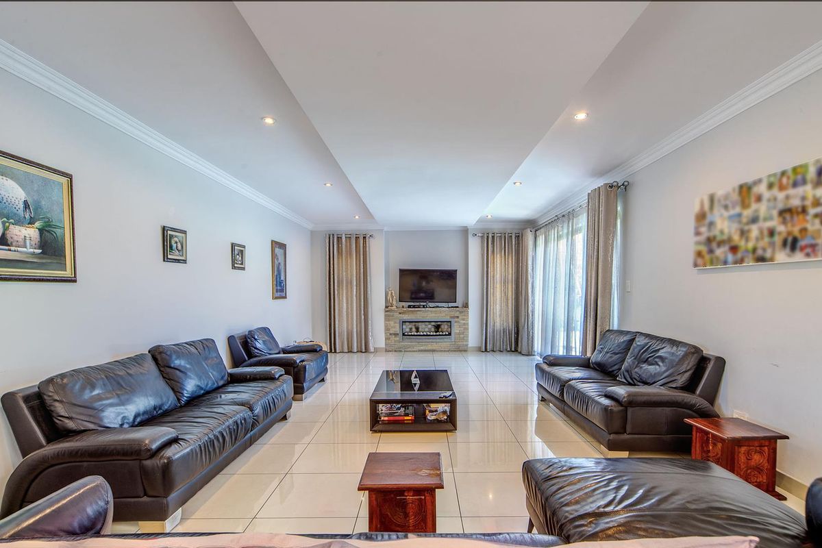 Spacious living room featuring large format floor tiles, recessed tray ceiling with downlights, and a central fireplace feature wall.