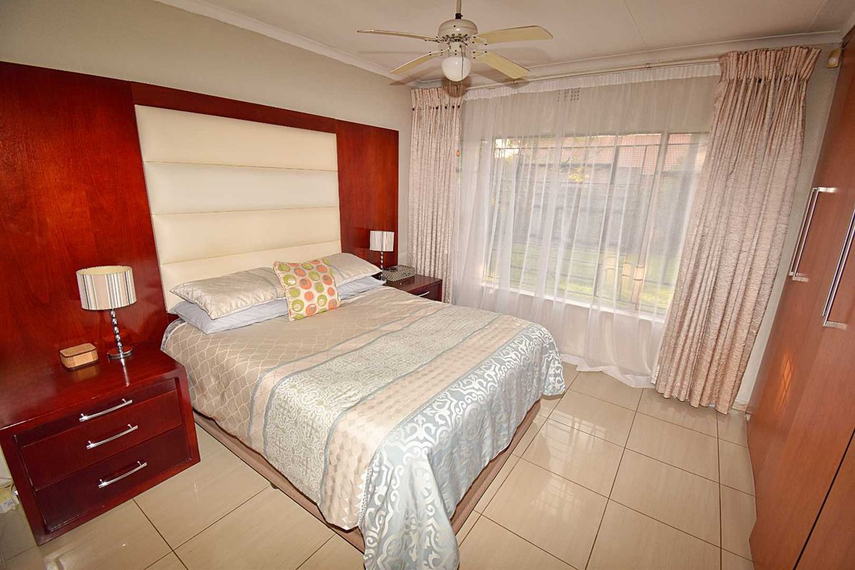 A well-maintained bedroom featuring built-in wooden cabinetry, a headboard, tiled flooring, and a ceiling fan.