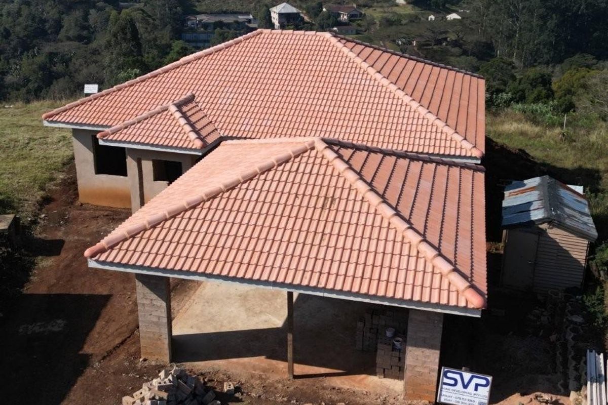 Aerial view of a residential property under construction, featuring a completed terracotta tiled roof and unfinished masonry structure.