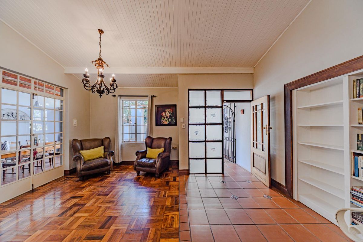 A spacious living area featuring a blend of parquet and terracotta tile flooring, beadboard ceiling, built-in shelving, and a decorative glass partition.