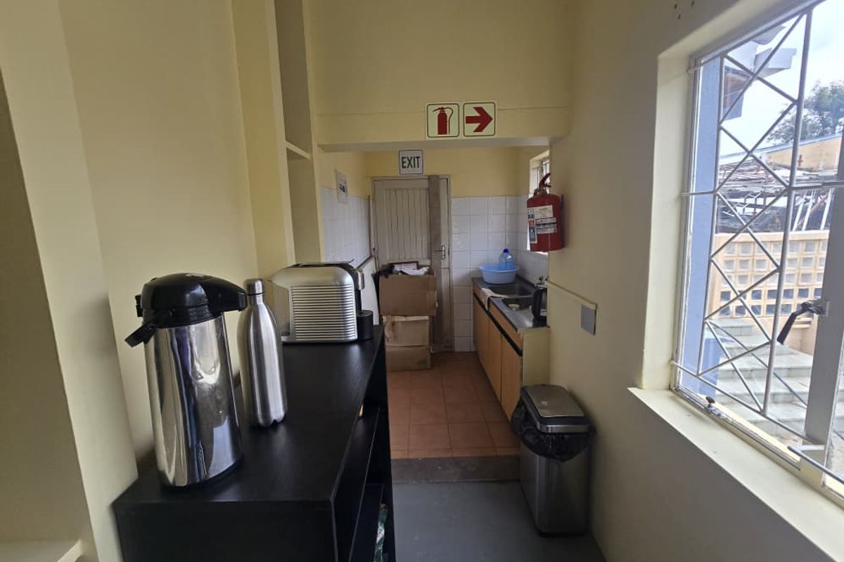 A functional office kitchenette featuring built-in cabinetry, a stainless steel sink, and a window providing natural light.