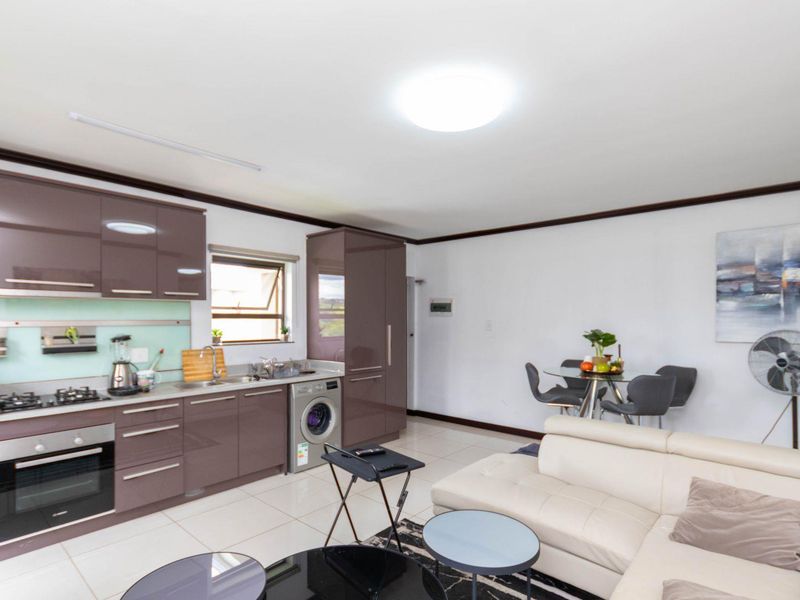 Open-plan living area featuring a modern kitchen with high-gloss cabinetry, integrated oven, gas hob, and tiled flooring throughout.