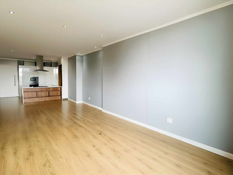 Spacious open-plan living area featuring modern laminate flooring, recessed lighting, and a sleek kitchen with integrated cabinetry and built-in appliances.