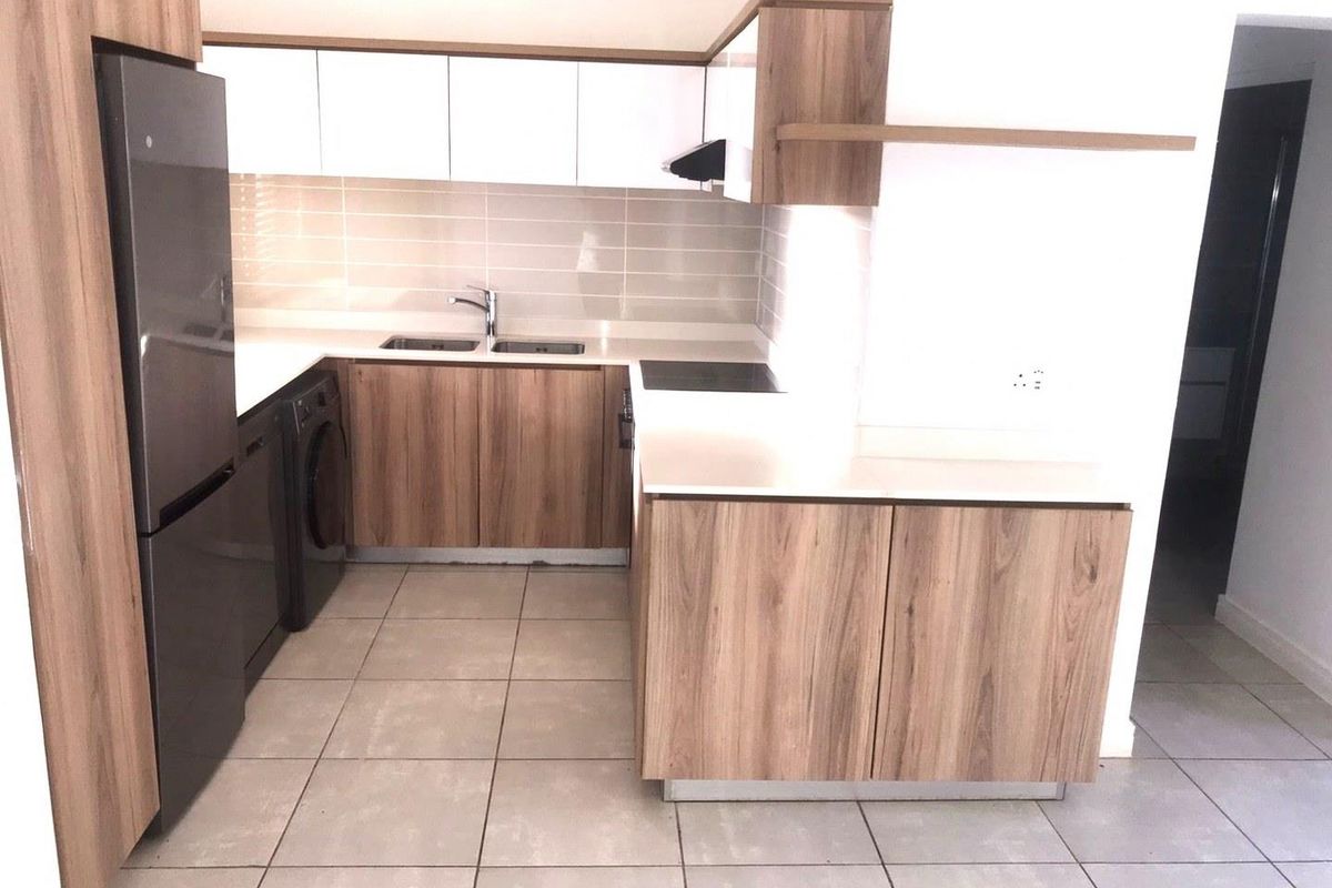 Modern kitchen featuring wood-grain cabinetry, white upper cabinets, stone-look countertops, tiled backsplash, and integrated space for appliances.