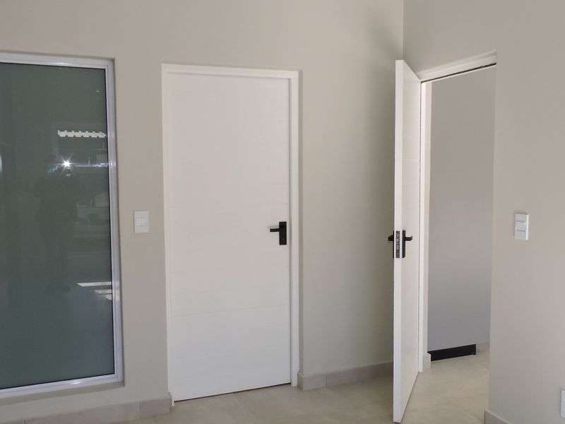 A clean, modern hallway featuring neutral walls, tiled flooring, and white internal doors with contemporary black hardware.
