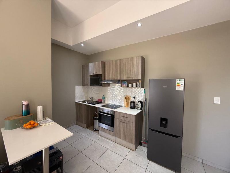 A modern, compact kitchen featuring wood-grain cabinetry, integrated appliances, tiled backsplash, and sleek tiled flooring, offering a functional and well-maintained cooking space.
