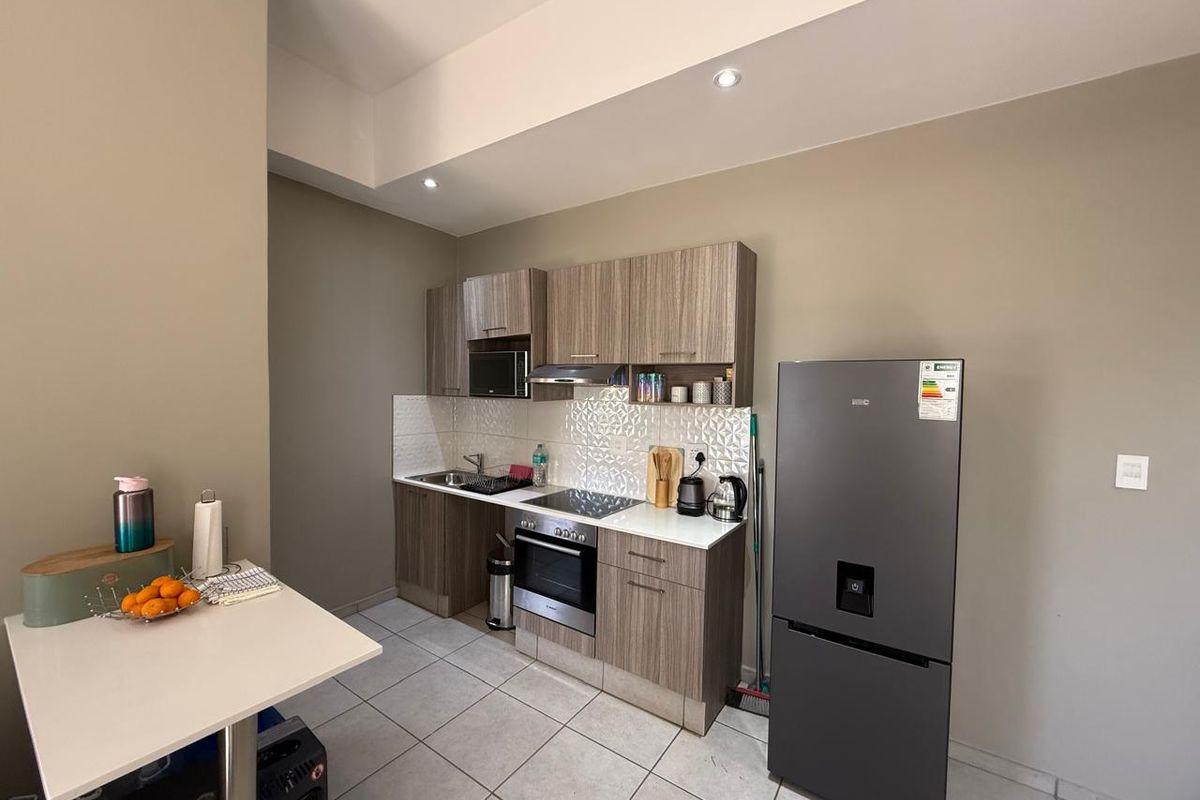 A modern, compact kitchen featuring wood-grain cabinetry, integrated appliances, tiled backsplash, and sleek tiled flooring, offering a functional and well-maintained cooking space.