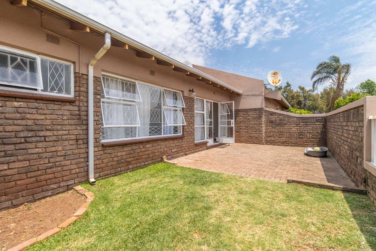 A private rear courtyard featuring a paved patio area, brick boundary walls, and a small lawn, accessible via glass doors from the main living space.