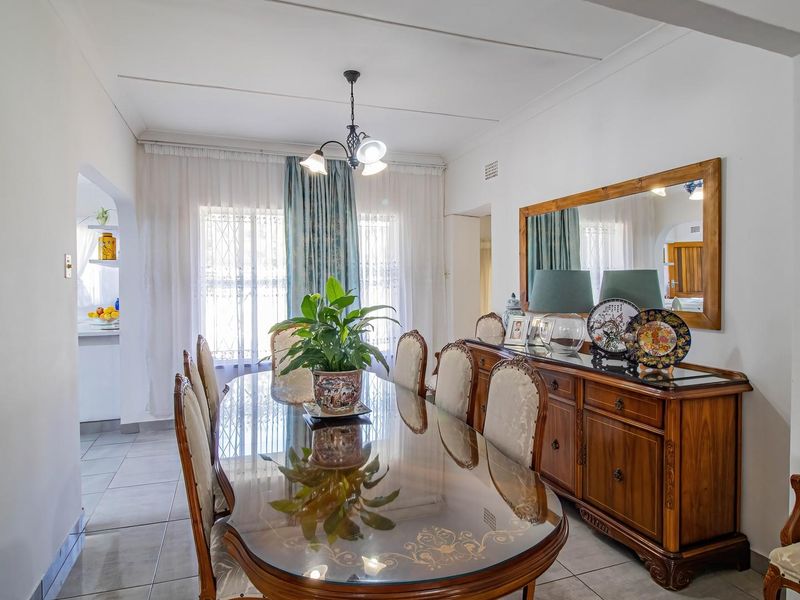 A well-lit dining room featuring tiled flooring and an open archway leading to the kitchen area.