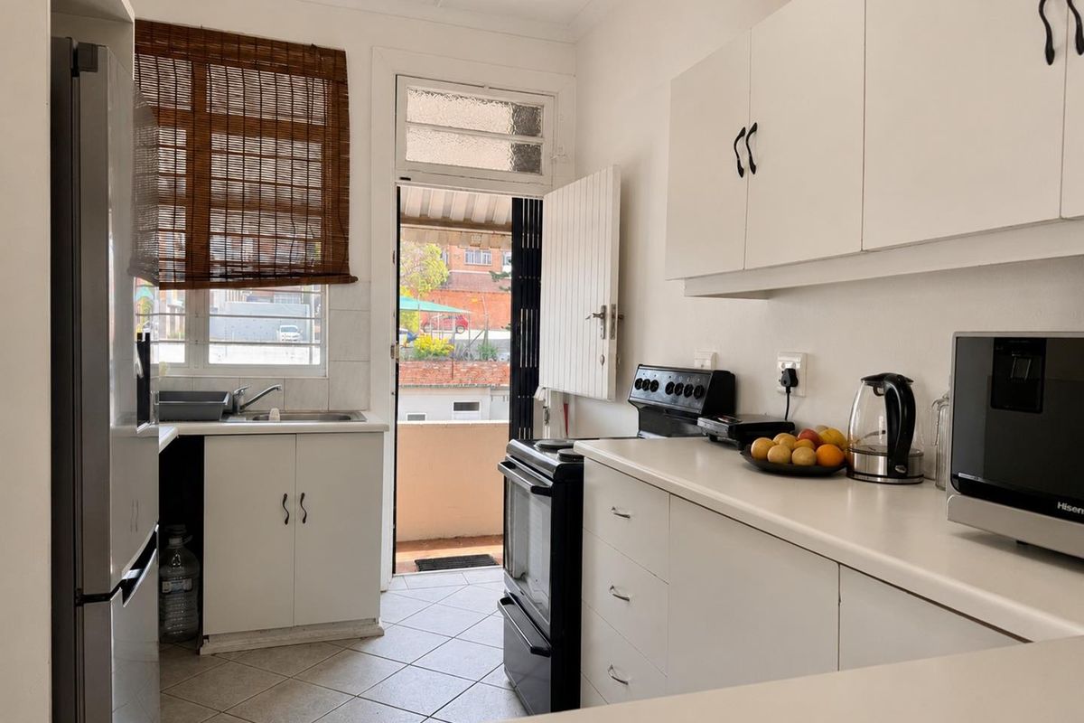 A functional kitchen featuring white cabinetry, laminate countertops, tiled flooring, and direct access to an outdoor balcony area.