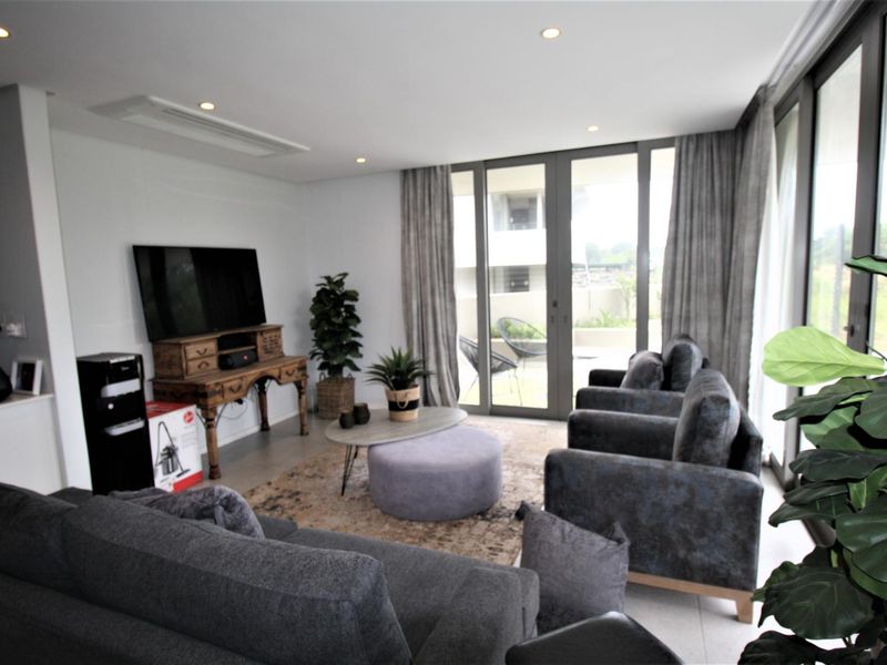 Modern living room featuring tiled flooring, recessed downlighting, ducted air conditioning, and large sliding glass doors providing access to the outdoor area.