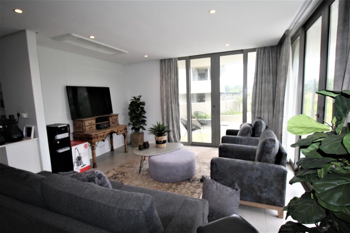 Modern living room featuring tiled flooring, recessed downlighting, ducted air conditioning, and large sliding glass doors providing access to the outdoor area.