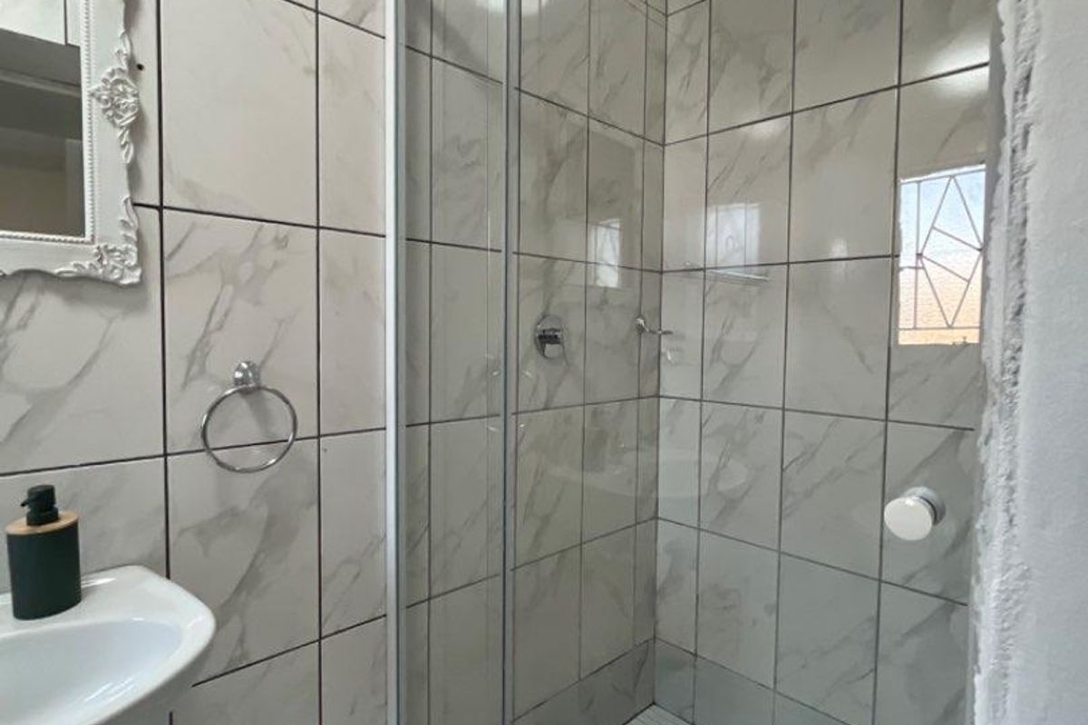 A modern bathroom featuring a glass-enclosed shower with marble-look wall tiles, a wall-mounted basin, and a chrome towel ring.
