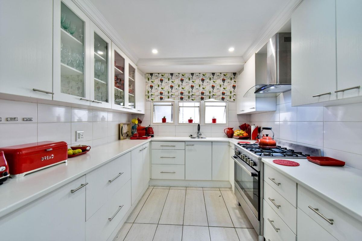 A well-maintained galley-style kitchen featuring white cabinetry, stone countertops, a gas hob, stainless steel extractor fan, and tiled flooring.