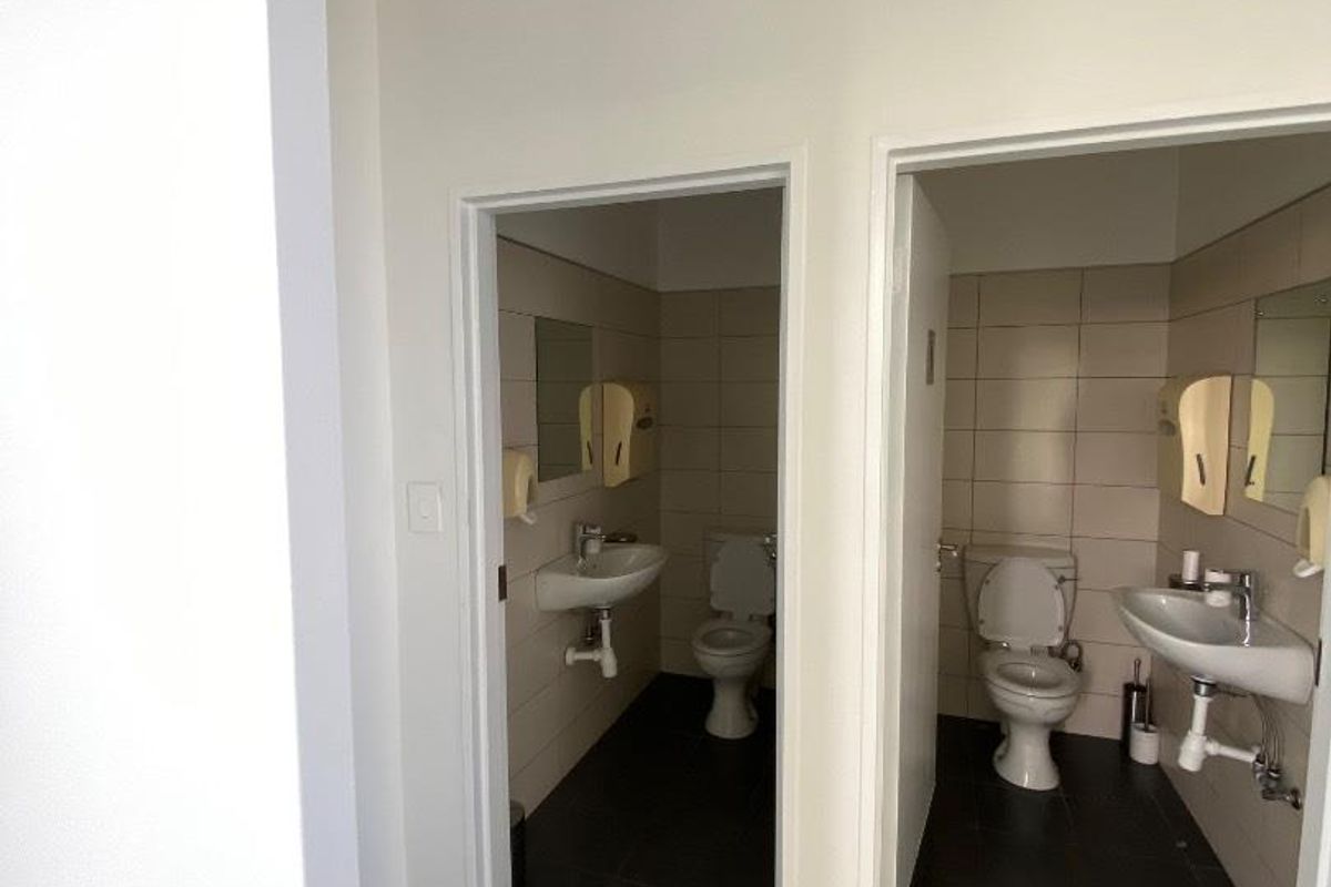 A functional office restroom facility featuring two separate stalls, each equipped with a wall-mounted basin and a standard toilet.