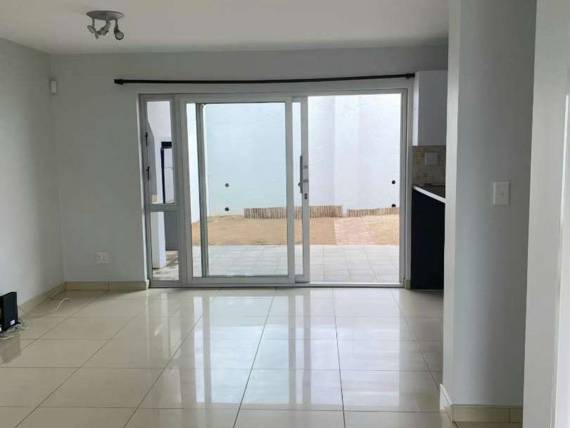 Bright open-plan living area featuring neutral tiled flooring and large sliding glass doors providing direct access to the rear patio and garden.