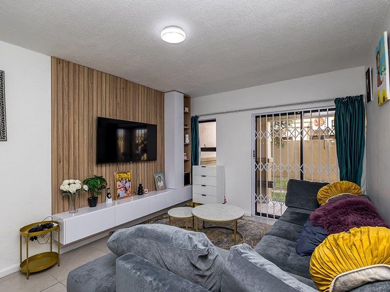 A well-maintained living room featuring a modern wood-look accent wall, built-in floating cabinetry, and a sliding glass door with security gate leading outdoors.