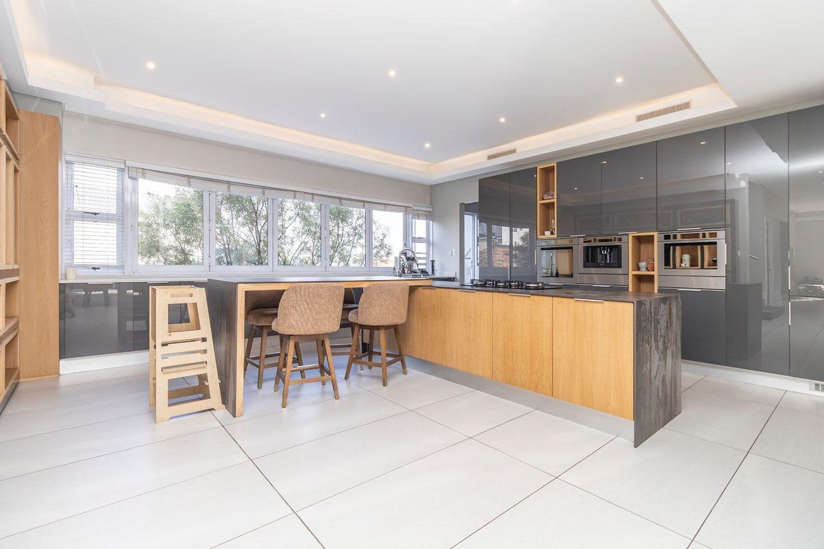 Modern kitchen featuring high-gloss cabinetry, a central island with integrated appliances, and large windows providing ample natural light.
