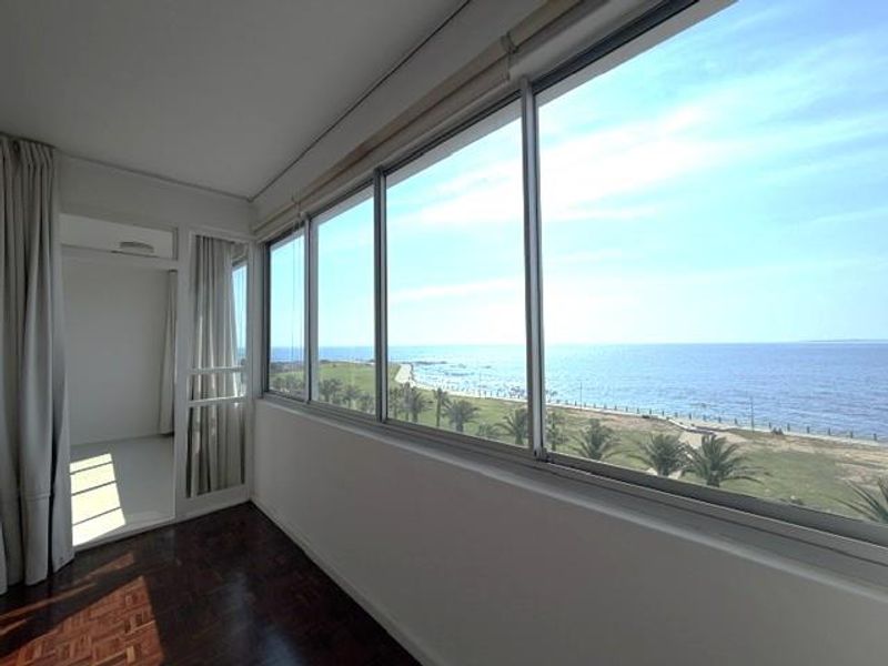 Enclosed balcony featuring parquet flooring and expansive windows offering panoramic ocean views, providing a bright and versatile space.