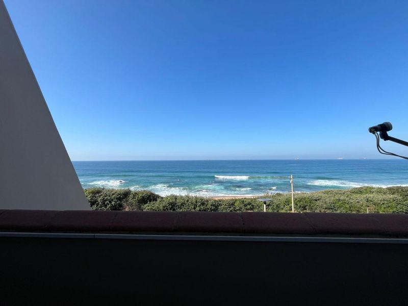 A clear, elevated view of the ocean and coastline from a balcony, showcasing the natural scenery and horizon.