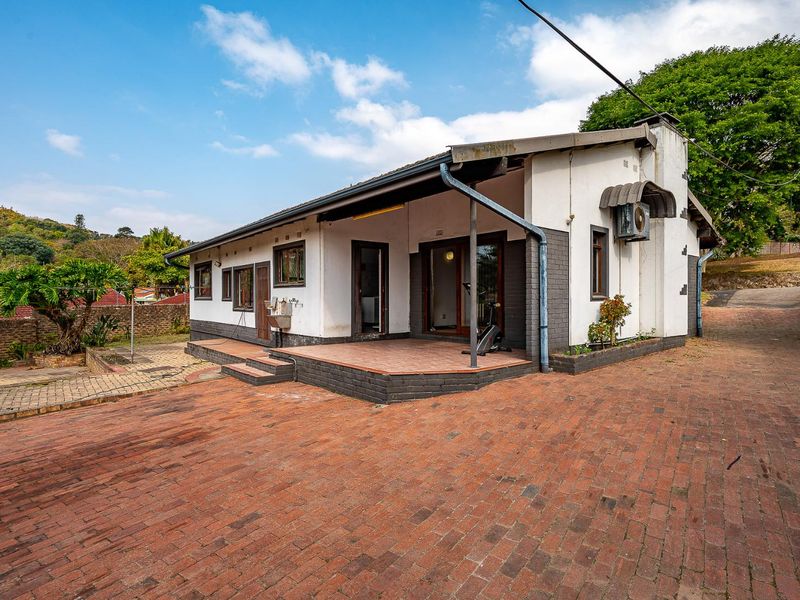 Rear view of the house featuring a paved driveway, covered patio area, and brick exterior finishes with established garden surroundings.