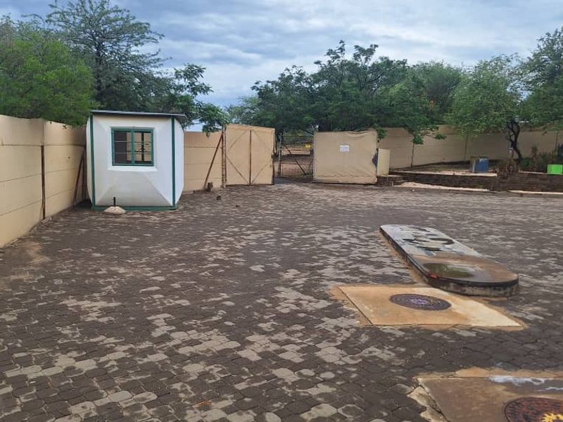 Industrial property entrance featuring a paved yard, perimeter wall, and a small security guard hut.