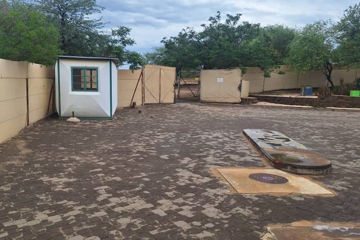 Industrial property entrance featuring a paved yard, perimeter wall, and a small security guard hut.
