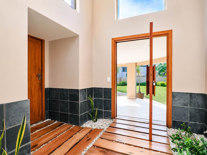 A bright and modern entrance hall featuring a striking timber pivot door, slate tile wainscoting, and unique timber slat flooring with decorative stone accents.
