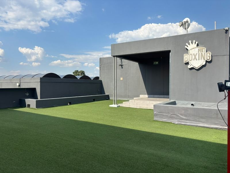 A spacious rooftop terrace featuring artificial turf, concrete steps, and exterior signage, providing an open-air area suitable for outdoor activities.