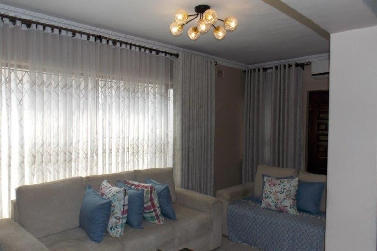 A comfortable living room featuring a modern ceiling light fixture, air conditioning unit, and large windows fitted with security gates and curtains.