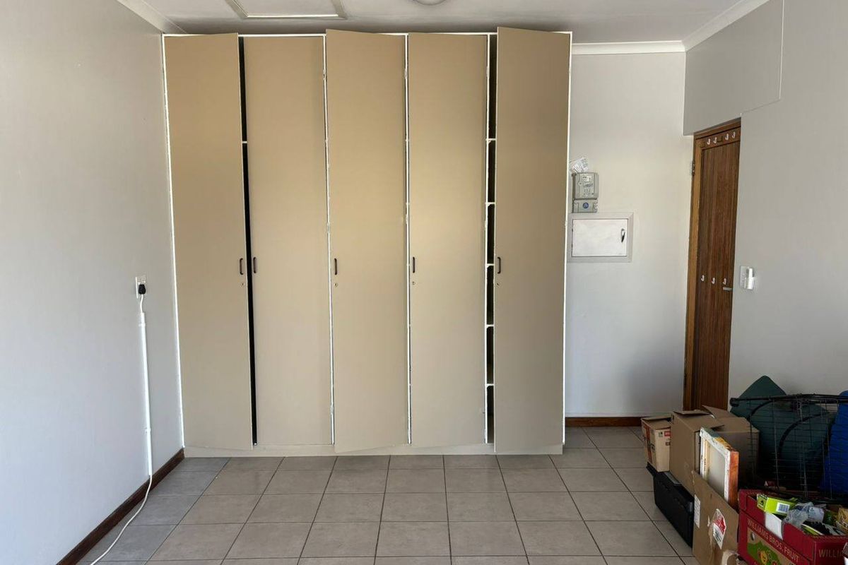 A bedroom featuring built-in floor-to-ceiling wardrobes, tiled flooring, and a standard wooden door.